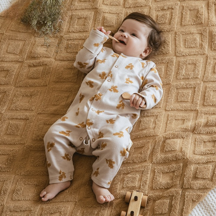 Adorable baby wearing a Gourbear vintage pattern Ear Of Wheat baby romper, lying happily on a blanket comfortably 